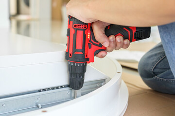 man assembling white table furniture at home using cordless screwdriver