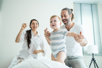 Caucasian loving parents play with baby boy child on bed in bedroom. 