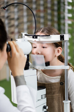 blurred optometrist testing vision of girl on autorefractor in optics salon.