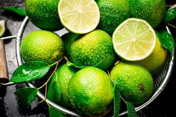 Fragrant lime with leaves in a colander. On a black damp background. High quality photo - obrazy, fototapety, plakaty