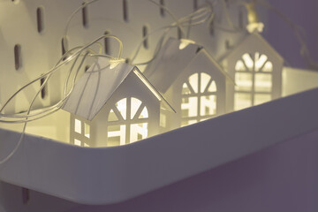 Electric garland in the form of white metal houses on a lilac wall. Christmas background