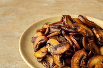 Heap of fried Champignon mushrooms on a plate. Brown edible fungi on a wooden table.