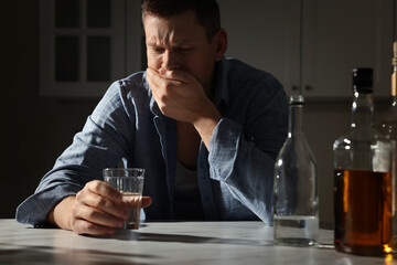 Addicted drunk man with alcoholic drink at table in kitchen