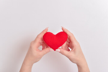 Obraz premium A red knitted heart in the hands of a girl with a beautiful manicure. Love. Organ donation. Pregnancy. Valentine's Day.