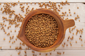 Uncooked organic buckwheat in a wooden cup on a wooden table, macro, top view.