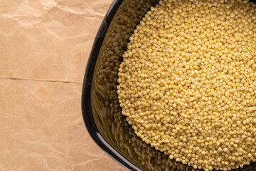 Raw organic millet groats in a black ceramic plate on craft paper, macro, top view.