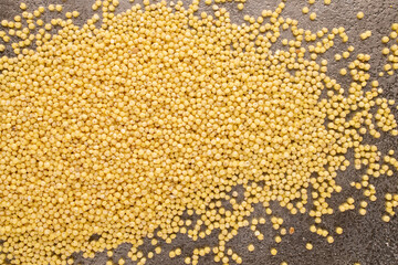 Raw organic millet groats on a metal tray, macro, top view.