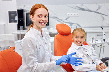 Smiling Female dentist is wearing gloves before curing teeth cavity, portrait. Dentist caries treatment for child girl at dental clinic office. People, medicine, stomatology and health care concept