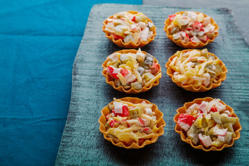 Salad with crab in tartlets on a black board.
