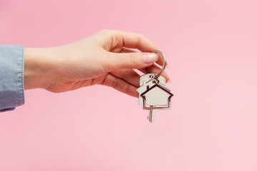 Female hand holding key and house keychain. Pink background with copy space. Concept of mortgage...