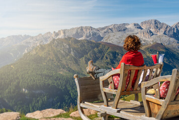 Mature woman sitting on a bench and enjoying the view of Italian Alps. Passo Rolle, Trentino - Italy
