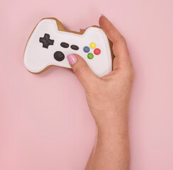 female hand holds gingerbread shaped game console on pink background