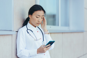 Sad doctor nurse Asian, near the clinic during a break, uses the phone, the woman has a severe...