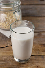 Dairy free oat milk in glasses and flakes in a bowl on wooden backgroun