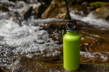 Camping steel bottle of water on a stone near mountain river