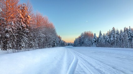 A road in the middle of a winter forest with a clear sky at sunset. Travel concept