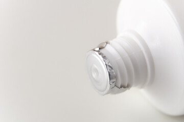 The tube of cream is sealed with protective foil. White tuba on a white background. Screw thread close-up. Copy space.