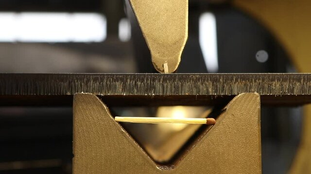 The bending machine bends a part from a thick sheet of steel with a match lying next to it to understand the dimensions of the products. Close-up. 