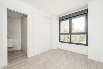 Room with built-in wardrobe with white sliding doors, en suite bathroom and large black aluminum window