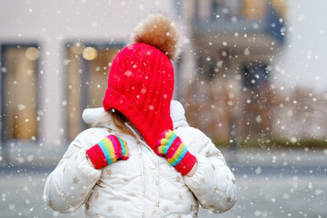 Funny portrait of little preschool girl in winter clothes. Happy positive child with red hat and colorful gloves outdoors. Winter day.