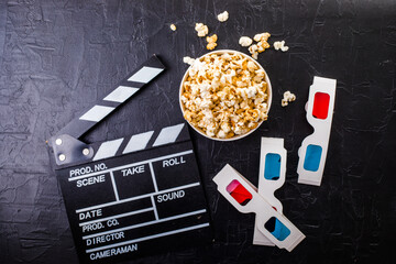 Cinema minimal concept. popcorn, 3d glasses clapper board on black background. Flat lay, top view