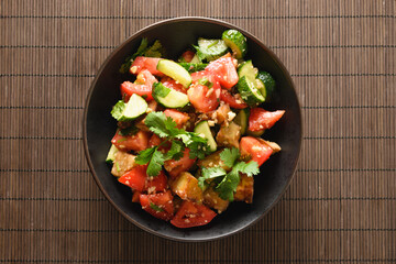 Chinese crispy spicy eggplant with tomatoes, cucumber, garlic, cilantro in oyster sauce and black vinegar isolated on brown mat. Chinese and Asian cuisine. Top view.