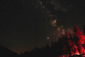 Fototapeta na wymiar Astronomy photo of the bright galactic cloud of the Milky Way stretches across the night sky over a remote mountainous and forested landscape in Yellowstone National Park