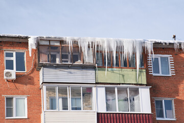 Balconies of an old residential brick house covered by the huge icicles. Dangerous icicles hangs...