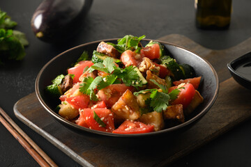 Chinese crispy spicy eggplant with cucumber, garlic, tomatoes, fresh cilantro leaves in oyster sauce and black vinegar on black background. Close up.