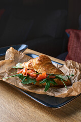 French croissant with salmon slices, avocado and spinach on blue plate on wood board background
