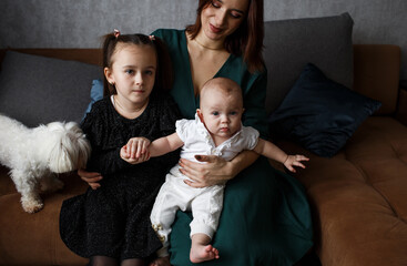 a happy young mother embraces two little daughters showing love and care sitting on the couch at home in the living room.