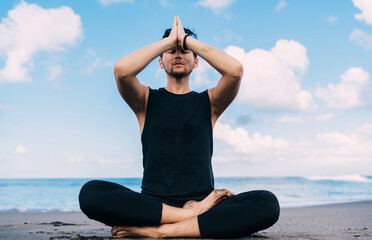 Calm Caucasian man with namaste keep praying during daytime at seashore beach enjoying leisure in Indonesia, young male yogi meditate in lotus pose searching soul enlightenment and mindfulness