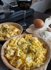 Side view of two plates of Nelga Rice along with various ingredients and a glass of red wine in the kitchen. Vertical.