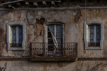 Casona abandonada en ruinas con el balc&oacute;n con las cortinas saliendo por los cristales rotos y dos ventanas