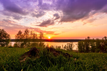 Naklejka na ściany i meble Beautiful scenic view at nice landscape on a beautiful lake and colorful sunset with reflection on water with green gras on foreground and glow on a background, spring season landscape