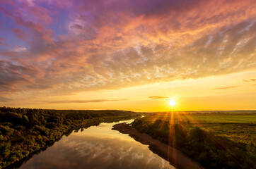 Scenic view at beautiful sunset or sunrise on a shiny river with green bushes on sides, golden sun rays, calm water ,deep blue cloudy sky and forest on a background, spring landscape