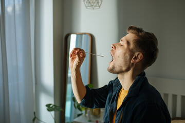 Man swabbing throat with home test for COVID-19. Coronavirus nasal swab test for infection. Rapid...