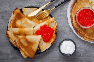 Stack of russian thin pancakes blini with red caviar and fresh sour cream.