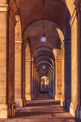Fototapeta na wymiar Outdoor arched corridor with columns in the Royal Palace of Madrid, Spain. Vertical architectural background with symmetrical outgoing perspective at sunset