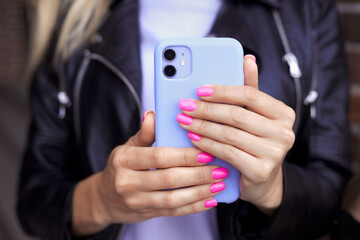 Closeup photo of female hands with bright neon pink manicure hold a smartphone in a purple case. No...