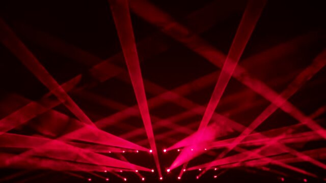 Colorful beams of red stage light in smoky dark studio. Red spotlights. Lighting equipment and light effects for design, concert hall and stage lighting during show or disco. Close up. Slow motion.