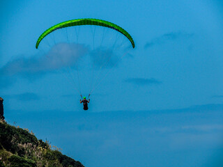Para glider soars over the beach, waves and hills at Murawai Beach, Auckland, New Zealand