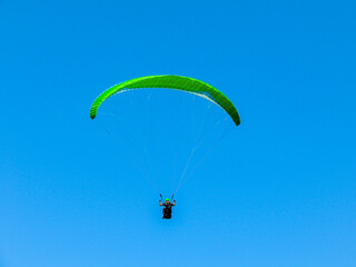 Para glider soars over the beach, waves and hills at Murawai Beach, Auckland, New Zealand