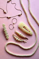 Various pearl jewelry and hair accessories on pink background. Flat lay.
