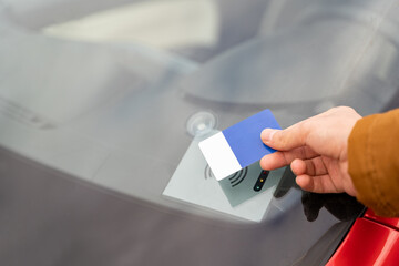 Male hand of young man holding modern electronic key card near computer on window of rental sharing car to open or close it. Travel, tour, tourism, journey, mode of transport, technology, ecology