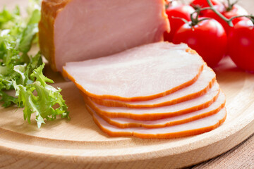 Sliced ham with tomatoes and lettuce on a wooden background