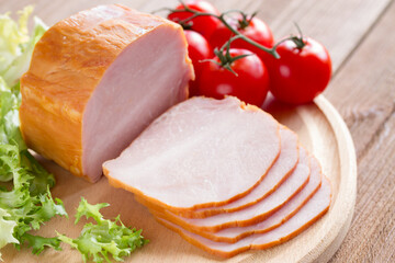 Sliced ham with tomatoes and lettuce on a wooden background