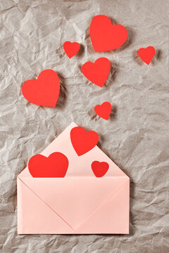 bright red heart-shaped cards fly out of the envelope on kraft paper. Love letter. Vertical photo