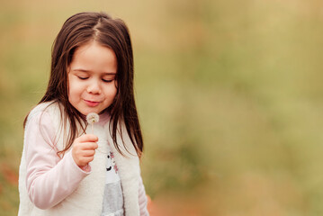 Little girl blowing a dandelion outdoors in the park