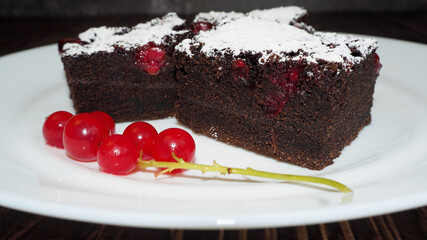 three pieces of gluten-free chocolate cakes with red currants, sprinkled with powdered sugar, lie on a white plate. gluten-free, lactose-free. homemade cakes